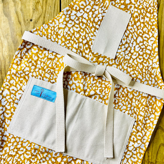 Apron with a leopard print pattern in shades of yellow, brown, and white, featuring a front pocket and an adjustable neck strap.