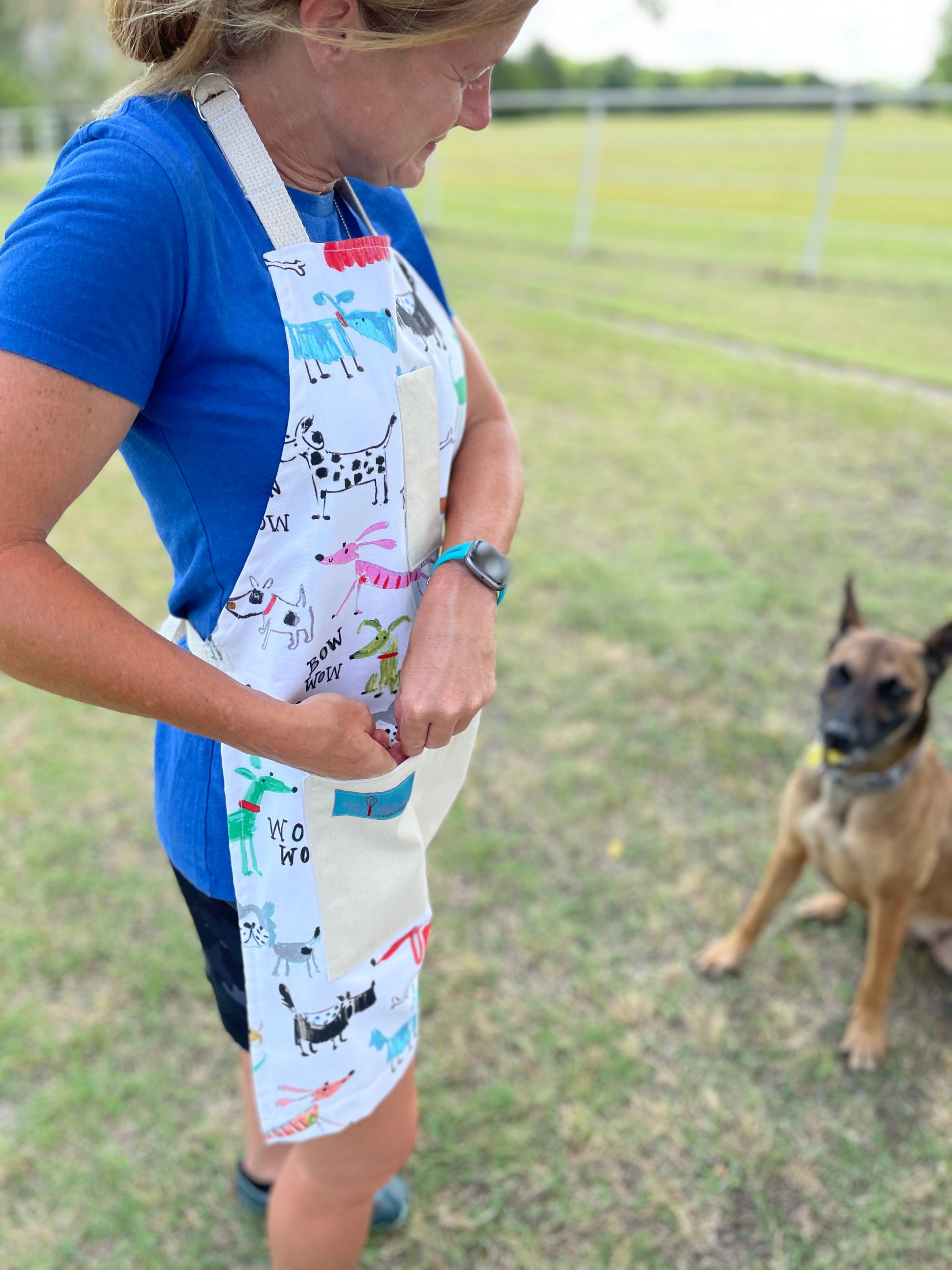 Two Medium Sized Ladies colorful playful dog apron Maribeth on dog trainer putting treats in pocket for pet