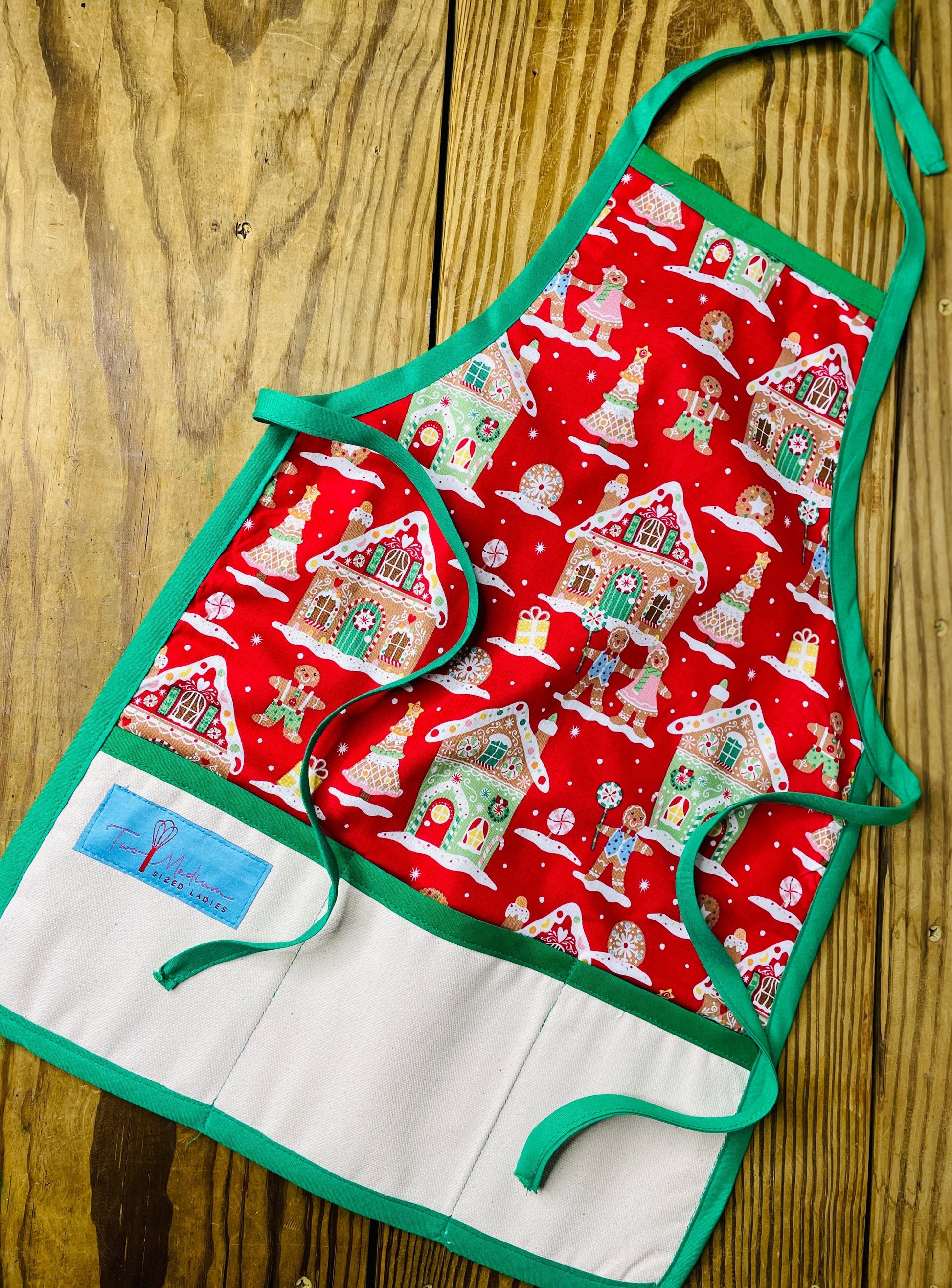 Two Medium Sized Ladies Children's Gingerbread House Gingerbread House Man Cookie Apron Red with Pink Details and Green Apron Strings