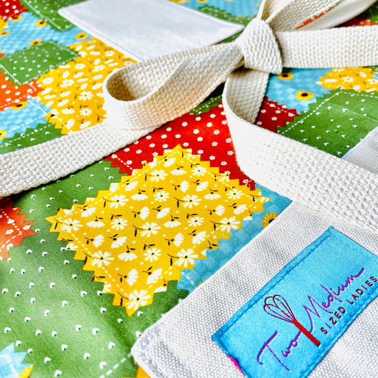 Two Medium Sized Ladies Maria Apron colorful patchwork quilt pattern in gold, green, cinnamon, burnt orange and aquamarine with sunflowers kitchen apron closeup view