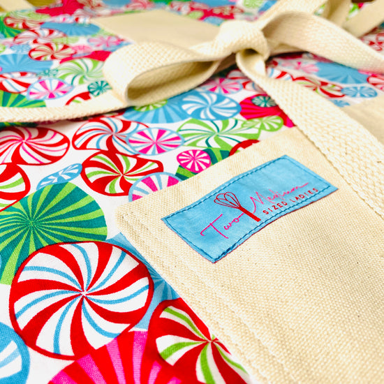 Two Medium Sized Ladies Peppermint Lane Apron close up view with sewn on label candy swirls Christmas baking cooking entertaining with family and friends