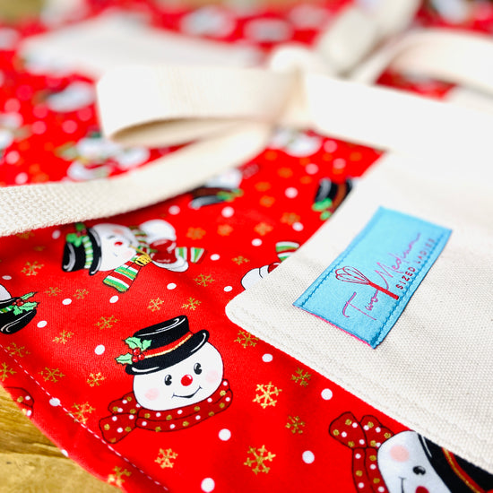Two Medium Sized Ladies frosty the snowman top hat holly leaf polka dot scarf apron on a red background with snow and gold reflective snowflakes