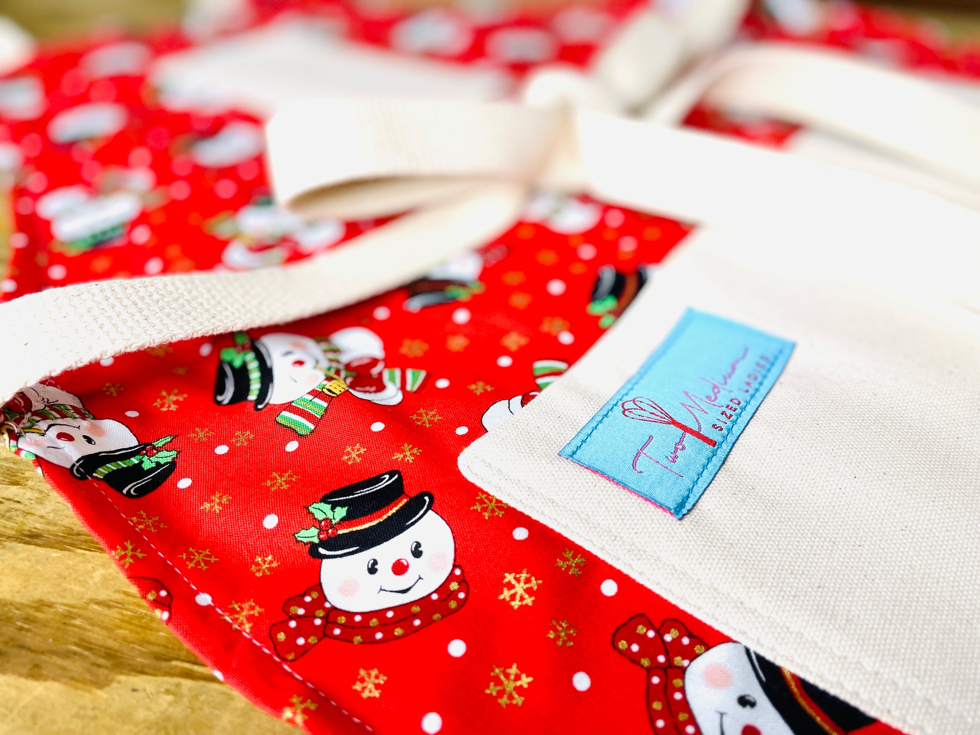 Two Medium Sized Ladies frosty the snowman top hat holly leaf polka dot scarf apron on a red background with snow and gold reflective snowflakes